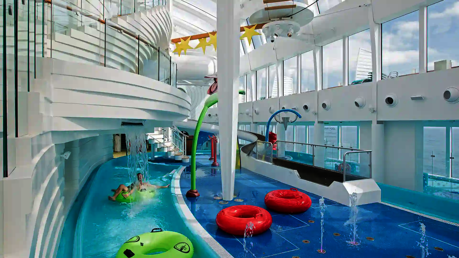 Lazy River im Indoor Bereich eines Kreuzfahrtschiffes mit Rutschreifen, Wasserattraktionen und bunten Spielgeräten.