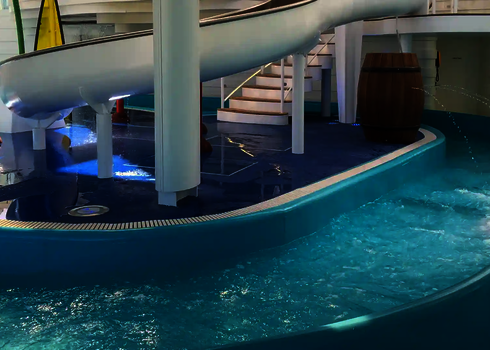 Wasser strömt durch den Lazy River vorbei an einer weißen Rutsche und Wasserspielen.