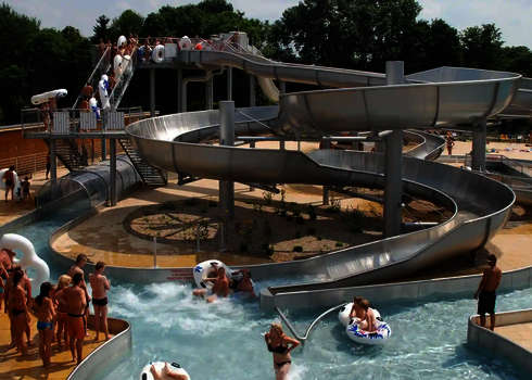 Wasserpark mit Badegästen, in der Mitte ein Rutschensystem aus Edelstahl.