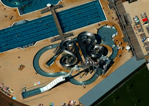 Luftaufnahme des Wasserparks mit einer Lazy River Rutsche, weiteren Edelstahl-Wasserrutschen und Schwimmbecken.