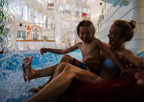 Mutter und Kind genießen eine Fahrt auf dem Lazy River mit Rutschreifen unter Wasserfall.