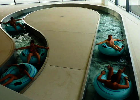 Mehrere Personen treiben auf Rutschreifen durch den Lazy River mit Panoramafenstern.